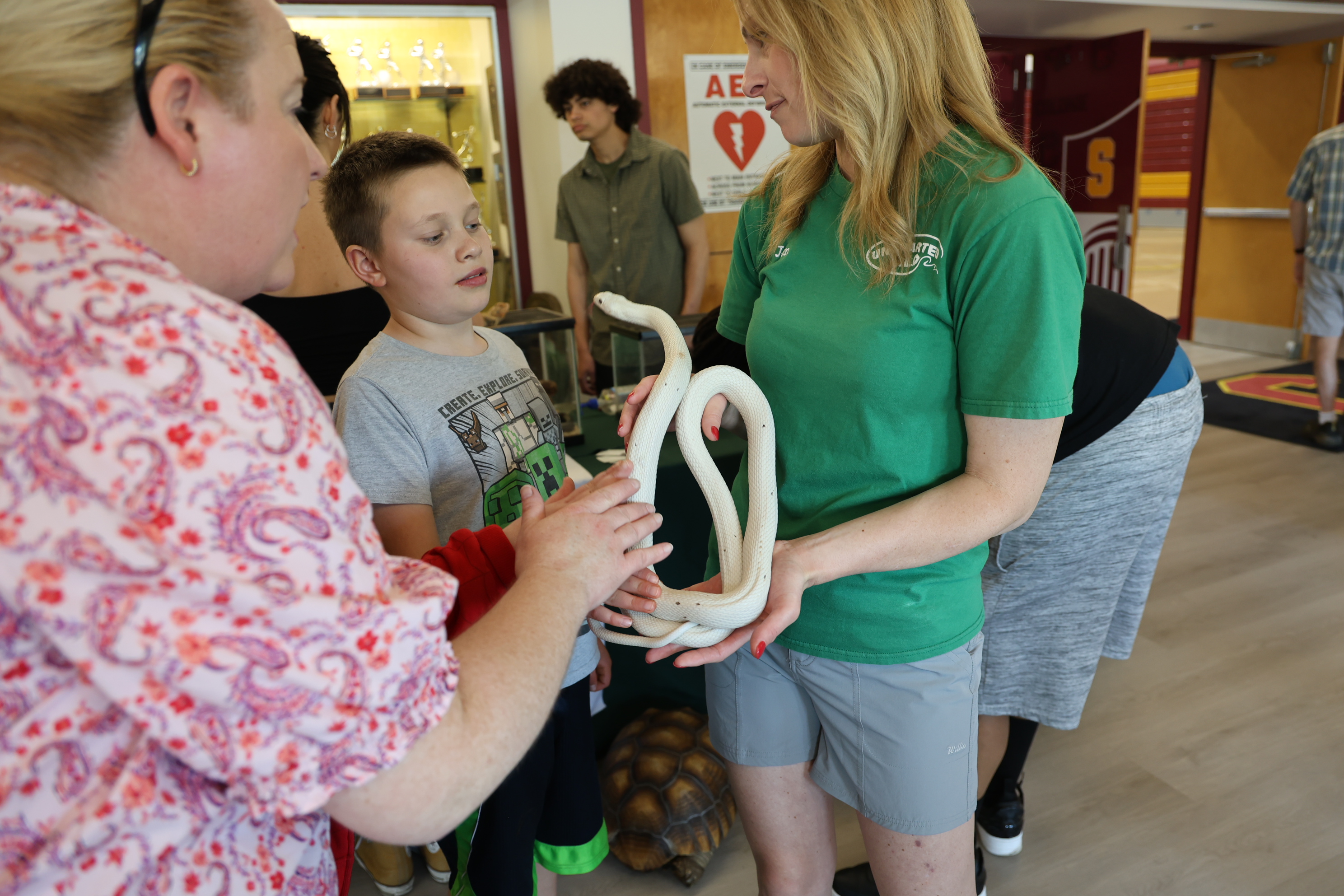 A woman wearing a green shirt shows a white snake to a student while standing with an adult